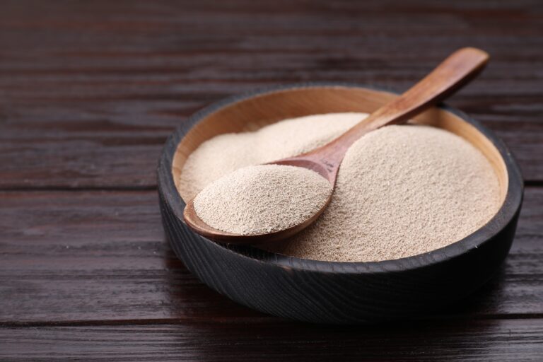 Bowl and spoon with active dry yeast on wooden table, closeup. Space for text for cleaning chemicals UK